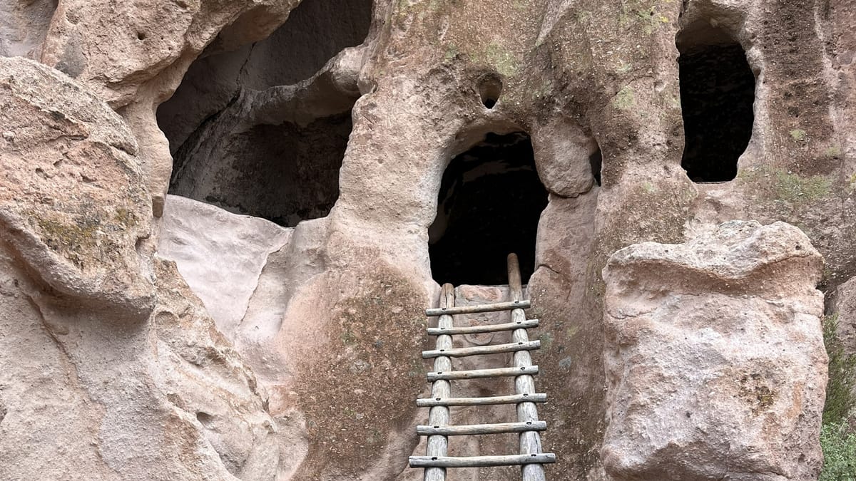 Three cave openings in a cliff with a ladder leading up to the middle one resemble the face of a skull